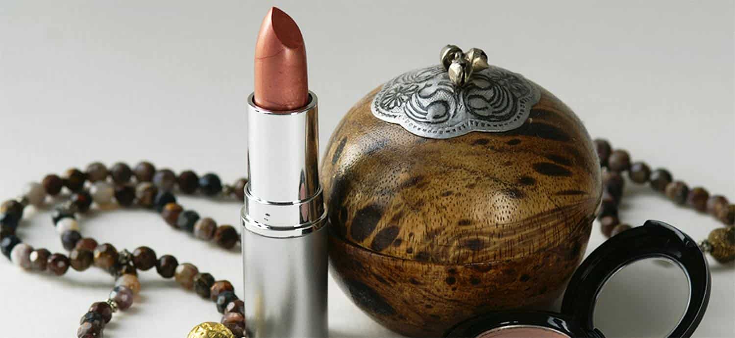 Lippenstift, Holzbehälter und Halskette auf weißem Hintergrund.