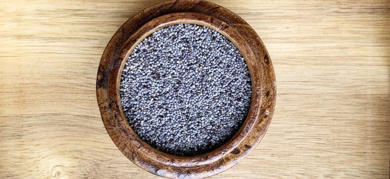 Holzschale mit schwarzen Mohnsamen auf Holztisch