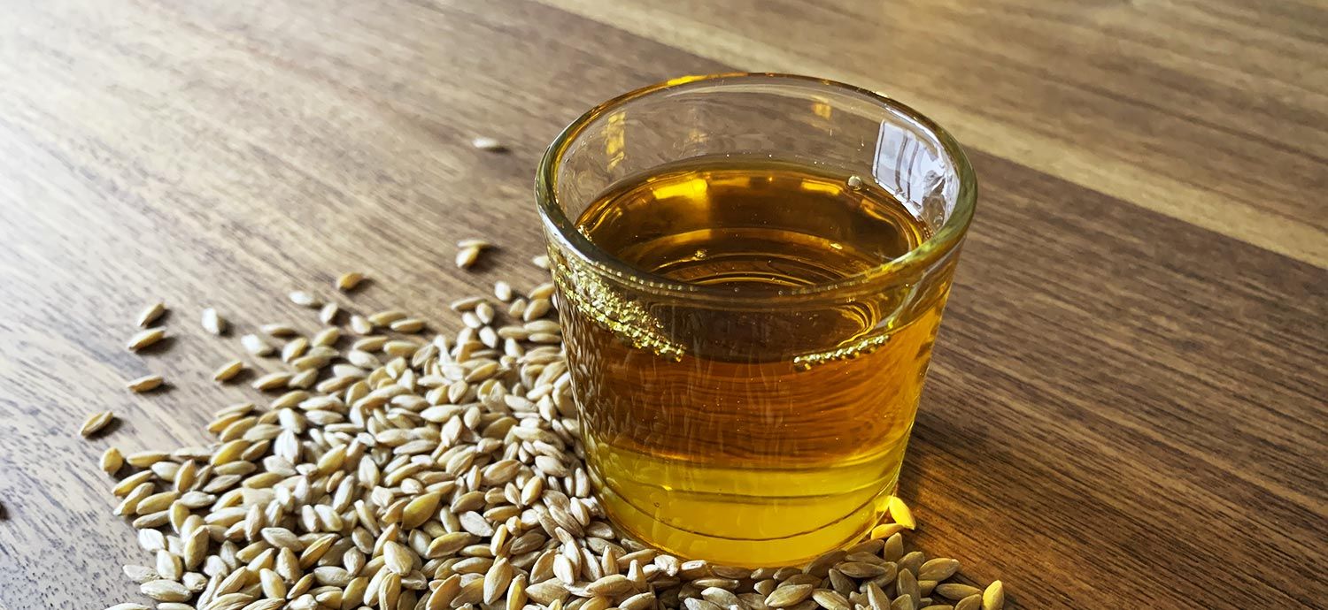 Glas mit goldenem Öl und Getreidekörnern auf Tisch.