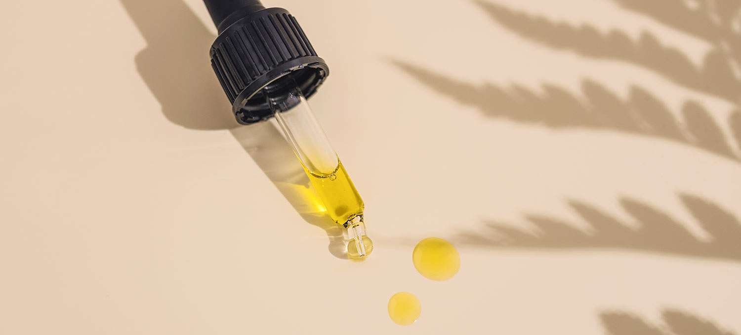 Pipette mit Öltropfen, auf einem hellen Untergrund liegend